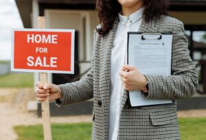 Real estate agent holding a Home for Sale sign and holding a purchase and sale agreement contract